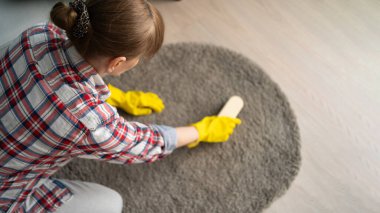 Ev manzarasında orta yaşlı bir kadın halı temizleme odasını fırçalıyor. Boşluğu kopyala