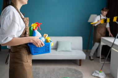 Kadın hademe oturma odasında bir sepet temizlik malzemesi tutuyor. Temizlik ve temizlik kavramı