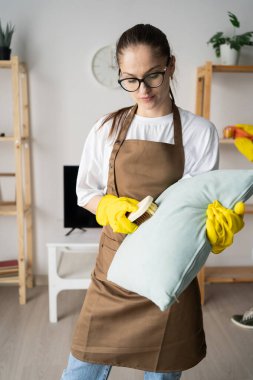 Kadın hademe oturma odasındaki yastığı fırçayla temizliyor. Boşluğu kopyala