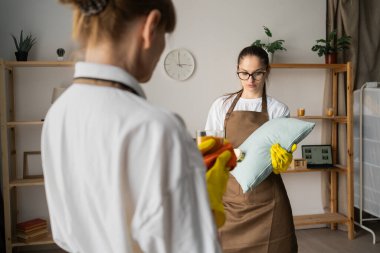 Bir temizlik ekibi, bir hizmetçi oturma odasında bir meslektaşla konuşurken yastığı temizliyor. Boşluğu kopyala