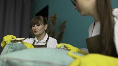 Temizlikçiler daireyi temizlerken kanepeden yastıkları fırçalarlar. Profesyonel temizlik hizmeti kavramı