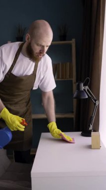 Sakallı adam temizlik için sprey deterjanı ve giysi ile iş yüzeyi konseptini temizliyor. Masa temiz. Dikey video