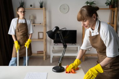 Temizlik hizmeti konsepti. Evde çalışan profesyonel temizlikçi kadın ekibi. Hizmetçi, masayı paçavrayla siliyor. Boşluğu kopyala