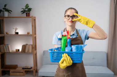 Önlük giyen kapıcı ve eldiven tutan eldiven ve temizleyici malzemelerle el ele tutuşarak V-İşareti veriyor. Boşluğu kopyala