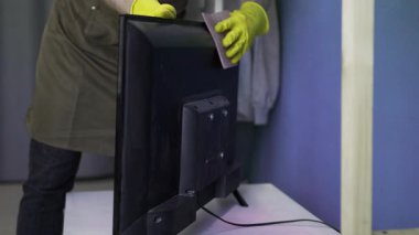 Erkek hademe, şık, rahat oturma odasında TV ekranını dikkatlice temizliyor. Ev temizliği, temizlik, ev temizliği, ev işleri ve temizlik hizmetleri konseptini temsil ediyor.