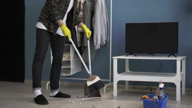 Sakallı adam süpürge ve süpürgeyle evdeki oturma odasında yerleri süpürüyor. Temizlik, ev işi ve temizlik konsepti