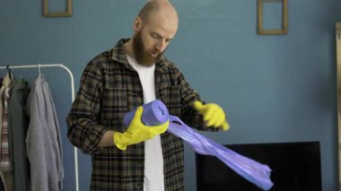 Ev temizliği sırasında plastik rulo siyah çöp torbasını parçalayan erkek temizleyici, ev işi, atık yönetimi, temizlik ve ev işi kavramını temsil ediyor