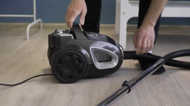 Ev temizliği konsepti. Adam yerleri süpürmeyi bitirdi ve temizlemek için elektrik süpürgesini söktü. Yakın plan.
