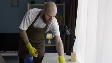 Sakallı adam masaları dezenfektan sprey ve bezle temizliyor. Oda servisi, ev işi ve ev temizliği konsepti