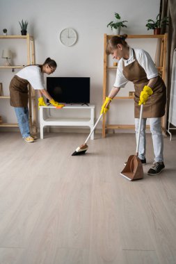 Temizlikçiler apartmanı temizliyor, oturma odasındaki televizyonu süpürüp tozluyor. Oda servisi, ev işi ve profesyonel temizlik konsepti. Uzayı kopyala Dikey görünüm