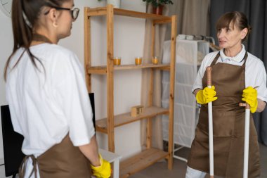 Ev işi ve temizlik konsepti. Profesyonel temizlik servisinden bayan hademeler dairedeki işi bitirdikten sonra ayakta duruyor ve konuşuyorlar. Boşluğu kopyala