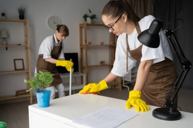 Müşteri dairesinde çalışan profesyonel hademeler evdeki hijyen bakımını, takım çalışmasını, sorumluluk ve temizlik hizmetlerini gösteren zemini silip süpürüyorlar.