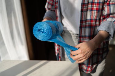 Kadın ellerinin plastik rulo çöp torbasını yırtması, ev atıklarının imhası, hijyen, çevre bakımı, geri dönüşüm ve günlük temizlik sorumluluklarını sembolize etmesi