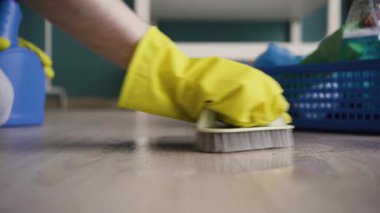 Erkek eli sarı eldiven giyerken, yerleri, ev işlerini ve temizlik konseptini fırçayla yıkarken yakın plan.
