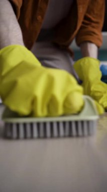 Kapalı alanda fırçayla yerleri temizleyen lastik eldivenli bir adam. Dikey video