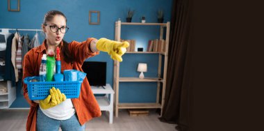 Kızgın kadın, elinde bir sepet deterjanla ekranı işaret ediyor. Evde temizlik yaparken negatif duygu, tasvip etmeme ve hayal kırıklığı gösteriyor. Boşluğu kopyala