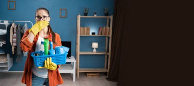 Şok olmuş bir kadın, evde temizlik koşullarında beklenmedik bir durumda saf şaşkınlık ve şaşkınlık içinde elini yüzüne koyup temizlik sepetini tutuyor. Pankart. Boşluğu kopyala