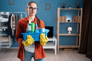 Çapraz kollu ve kızgın yüzlü bir kadın elinde somurtkan ruh hali, hayal kırıklığı ve aile içi çatışma duygularını gösteren deterjan sepeti tutuyor. Boşluğu kopyala