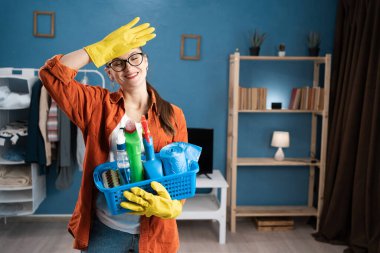 Eldiven takan, gülümseyen ve alna dokunan bir kadın ev işi sonrası deterjan ile temizlik, temizlik, rahatlama, memnuniyet ve rutin konsepti gösteriyor.