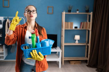 Parmağını kaldırmış ve elinde temizlik malzemesi sepeti tutan ilham verici bir kadın. Evinde harika bir fikir ve yaratıcı düşünce var. Boşluğu kopyala