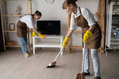 Temizlikçiler apartmanı temizliyor, oturma odasındaki televizyonu süpürüp tozluyor. Oda servisi, ev işi ve profesyonel temizlik konsepti. Boşluğu kopyala.