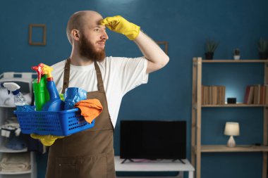 Temizlik malzemeleriyle dolu sepeti tutan sakallı hademe elleri başının üzerinde başka yere bakıyor. Temizlik, temizlik ve ev işi konsepti