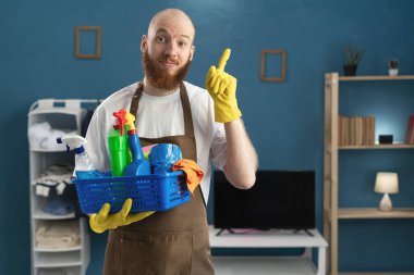 Pozitif gülümseyen, sakallı, önlük takan, temizlik malzemesi taşıyan sakallı adam iyi fikir jestini işaret ediyor. Temizlik, temizlik ve ev işi konsepti