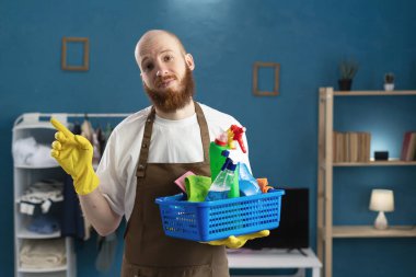 Kapıcı sakallı adam, elinde önlükle temizlik malzemeleriyle solu işaret ediyor. Temizlik, temizlik ve ev işi konsepti
