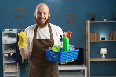 Kapıcı sakallı adam elinde önlükle temizlik malzemelerini tutarken heyecanlı kollarıyla birinci sınıf jest yapıyor, galibiyeti kutluyor. ev işi kavramı