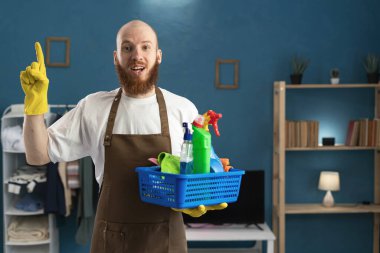 Neşeli, sakallı, önlük giyen, temizlik malzemesi taşıyan, fikir jesti yapan, zaferi kutlayan neşeli hademe sakallı adam. ev işi ve temizlik konsepti