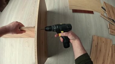 POV, tahta yonga tahtasına vida vidası takmak için tornavida kullanıyor. Modern bir mutfak dolabındaki hassas mobilya montajı, yeni odada güçlü bir kurulum için gerekli parçaları donanım sağlıyor..