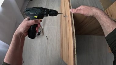 Mobilya montajı için kablosuz tornavida kullanarak ev geliştirme becerileri. Sanatçı bir dolap kuruyor, matkapla vidaları sıkıyor, masanın iki parçasını birleştiriyor..