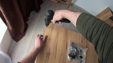 Onaylanmış bir vidayı tornavidayla tahta dolaba vidalayan elleri kapatın. Mutfak dolabını kuruyorum. Elektrikli matkapla vidaları sıkmak, tezgahın iki parçasını birbirine vidalamak..