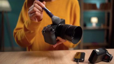 Kadın fotoğrafçı tozu kaldırmak için yumuşak fırça kullanarak kamerayı nazikçe temizliyor, ideal performans için profesyonel bakım ve fotoğraf ekipmanlarının bakımını gösteriyor