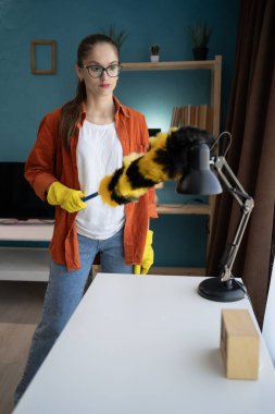 Esmer kadın ev temizliği, temizlik, hijyen, nazik yüzey bakımı ve ev temizliği kavramını gösteren toz beziyle masa lambasının tozunu alıyor.