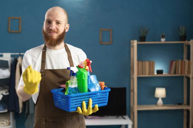 Yakışıklı, sakallı, kel bir adam temizlik malzemelerini tutuyor ve oturma odasında dikilirken parmaklarıyla flört ederek yaklaşmaya çalışıyor. Ev işleri, ev işleri, ev işleri ve temizlik.