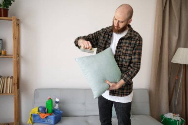 Ev temizliği yaparken günlük gömlekli yetişkin adam yastık fırçalarken ev işleri ve ev işleri kavramı