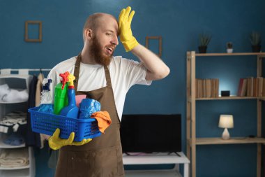 Stresli, kötü duyguları olan genç bir adam elinde renkli temizlik malzemeleriyle sepeti oturma odasında duruyor. Temizlik hizmeti kavramı