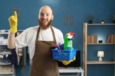 Önlüklü mutlu sakallı adam elinde temizlik malzemeleriyle kameraya gülümsüyor. Düşünce jestleri yapıyor, dahi çocuk. Boşluğu kopyala