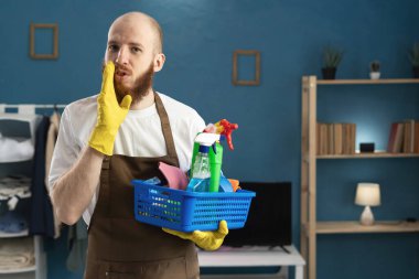 Kameraya fısılda. Gizli ve dedikodu konsepti. Genç adam oturma odasında bir sepet temizlik malzemesi tutuyor. Boşluğu kopyala