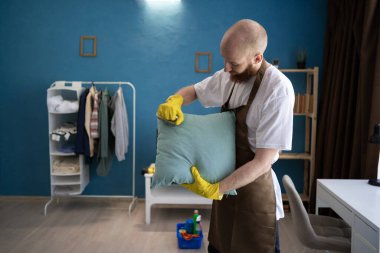 Kapıcı, evdeki oturma odasında fırçayla yastığı temizliyor. Ev işleri ve ev işleri konsepti