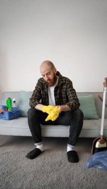 Adam oturma odasında kanepede otururken temizlik için sarı lastik eldiven giyiyor. Ev işleri. Boşluğu kopyala