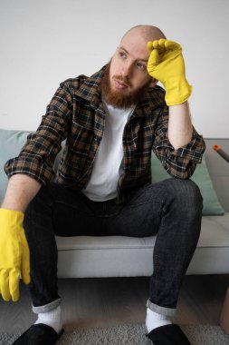 Temizlikten sonra eli kanepede dinlenen yorgun ve sakallı bir adam. Yakın plan.