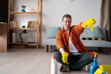 İnsanların yaşam tarzı konsepti. Üzgün genç bir kadın, sarı eldivenler giyer. Elinde temizlik malzemeleriyle otururken hoş olmayan davranışlar sergiler. Boşluğu kopyala