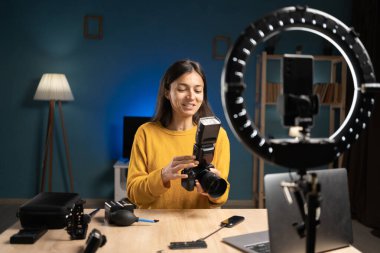 Kadın fotoğrafçı içerik yaratıcısı sosyal medya için akıllı telefonu kullanıyor, video blokluyor, canlı yayın yapıyor. Etkilendirici fotoğrafçı kamerayı flaş ile gösteriyor, ipuçları veriyor, eğitici podcast sunuyor.