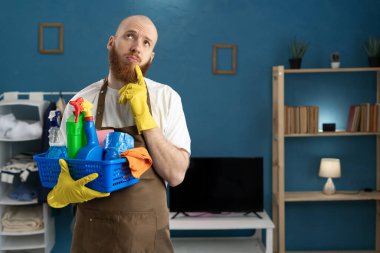Düşünceli temizlik servisi çalışanı elinde sepetle temizlik ürünleriyle yeni iş fikrini düşünüyor. Ev işleri, ev işleri ve ev işleri.