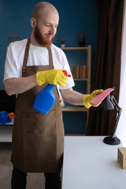 Temizlik, angarya ve temizlik. Sakallı bir adam sprey şişesinden deterjan püskürtüyor. Ev temizliği, kopyalama alanı