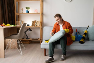 Kanepede oturan kadın temizlik fırçasıyla yastığı fırçalıyor. Ev temizlik rutinini, tekstil bakımını, günlük işleri ve ev işleri ve ev işleri kavramını gösteriyor.