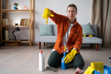 Genç kadın ev temizliği deterjan ürününü işaret ediyor. Ev hanımı dairesini topluyor temizlik malzemeleriyle yerde oturuyor, ev işlerini yapıyor. Boşluğu kopyala