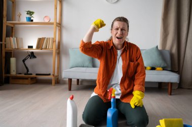 Genç kadın ev temizliği zaferi kutluyor. Ev hanımı dairesini topluyor temizlik malzemeleriyle yerde oturuyor, ev işlerini yapıyor. Boşluğu kopyala